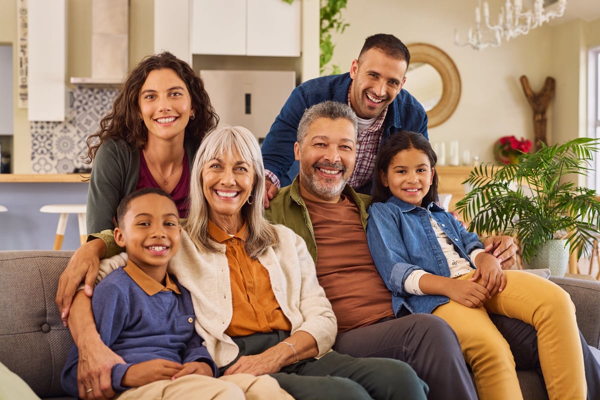 Portrait of happy family with grandmother and grandfather sitting on couch at home. Smiling parents, grandparents and happy multiethnic children looking at camera. Cheerful mixed race extended generational family having fun in the living room while smiling.